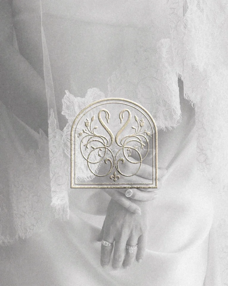 Ivory embossed swan monogram held against a lace wedding dress