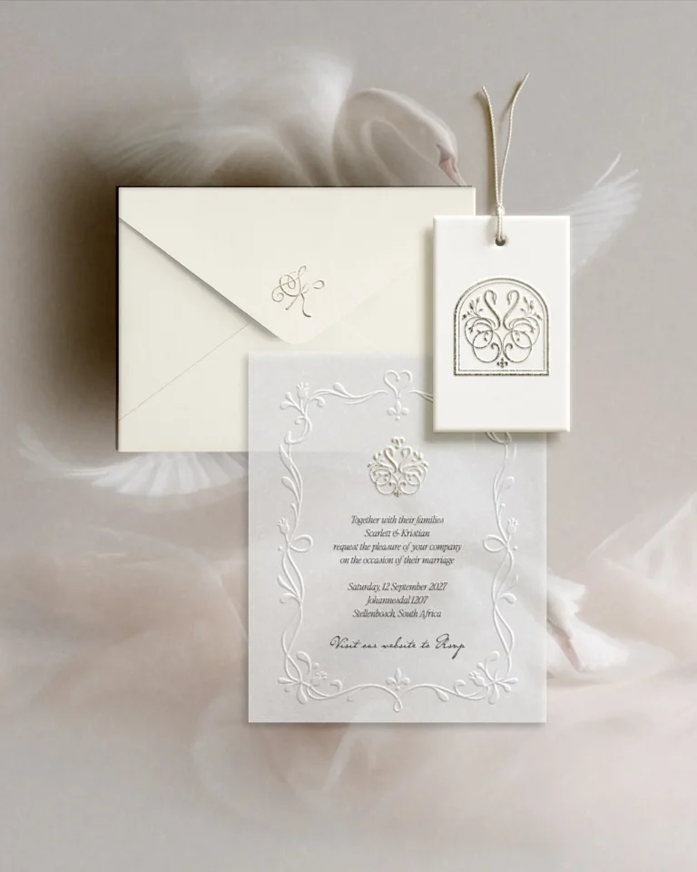 Ivory letterpress wedding invitation, envelope and swan monogram tag resting on soft tulle