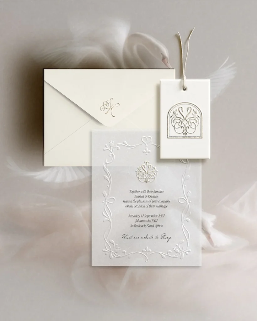 Ivory letterpress wedding invitation, envelope and swan monogram tag resting on soft tulle