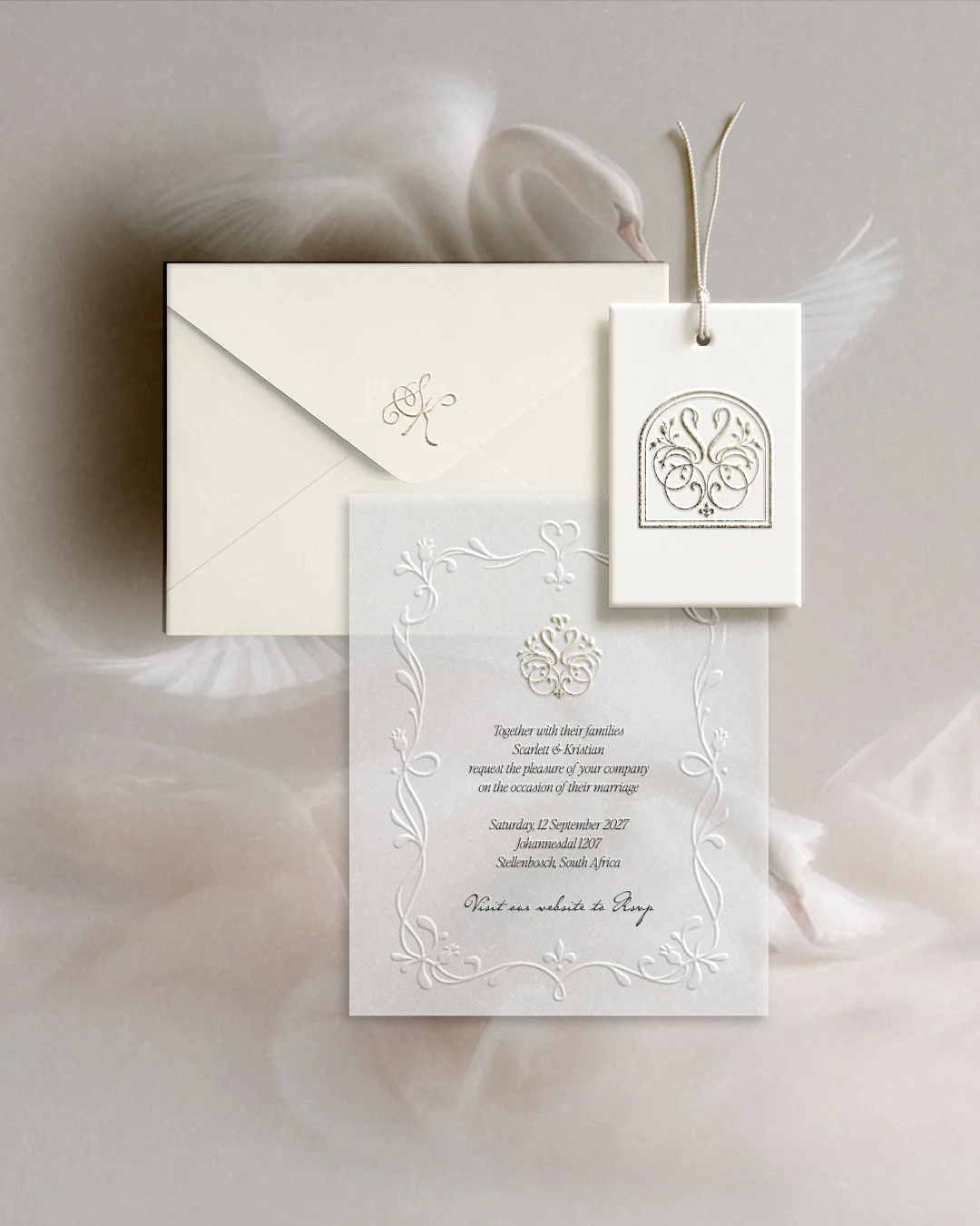 Ivory letterpress wedding invitation, envelope and swan monogram tag resting on soft tulle